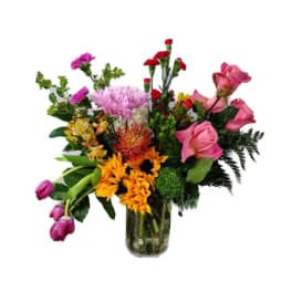 Mixed bouquet of pink roses, orange flowers, and red carnations in a glass vase