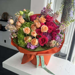 Vibrant hatbox arrangement with hot pink roses, peach spray roses, green hydrangeas and pastel blossoms