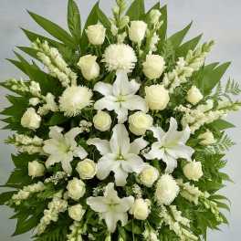 Standing spray of white lilies, roses, and other blooms with large green leaves on an easel