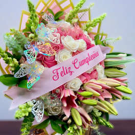 Tall arrangement of pink lilies and pink and white roses with a Feliz Cumpleaños ribbon and butterfly accents.