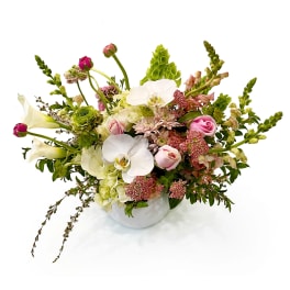Lush arrangement of white orchids, calla lilies, and pink roses in a round white vase