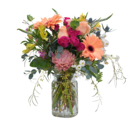 Mixed bouquet of peach gerbera daisies, pink roses, and assorted blooms in a clear glass jar vase