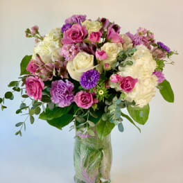 Mixed bouquet of pink, white, and purple flowers in a clear glass vase lined with green leaves