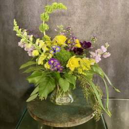Mixed bouquet in a clear glass vase with yellow, purple, pink, and dark blooms