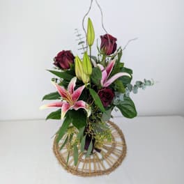 Bouquet of pink lilies and dark red roses with greenery in a woven base