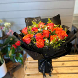 Bouquet of orange roses with small white filler flowers in black wrap