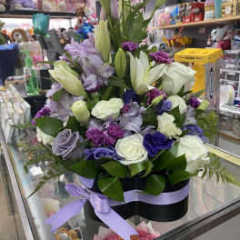 Lavender and white flower arrangement with roses, lilies, and carnations in a black hatbox with purple ribbon
