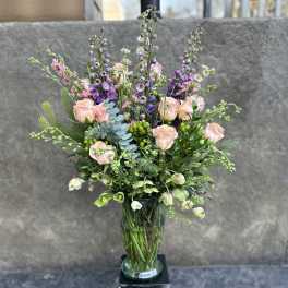 Tall bouquet of blush roses and purple flowers in a glass vase