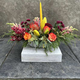 Colorful floral centerpiece with a tall yellow candle in a low container