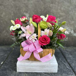 Pink roses and lilies arranged in a wooden basket with a pink ribbon