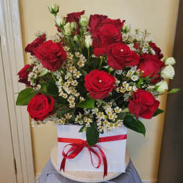 Red roses and white filler flowers in a white box with a red ribbon