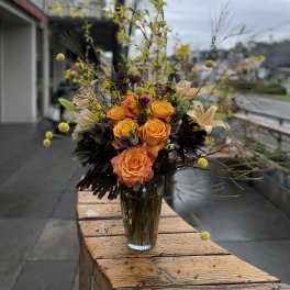 Orange roses in a clear glass vase with airy yellow accents