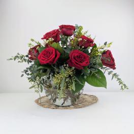 Red roses arranged in a clear glass vase with greenery