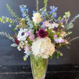 Mixed bouquet in a clear glass vase with white, blue, and pink flowers