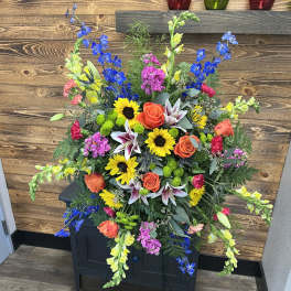 Large standing floral spray with sunflowers, roses, lilies, and blue delphinium