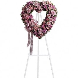 Heart-shaped pink rose wreath on a white stand with ribbon
