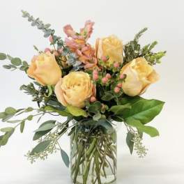 Peach roses arranged in a clear glass vase with mixed greenery