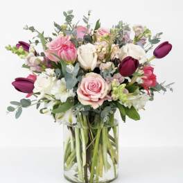 Mixed bouquet of pink, white, and burgundy flowers in a clear glass vase