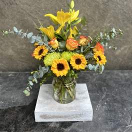 Yellow lilies and sunflowers in a glass jar vase