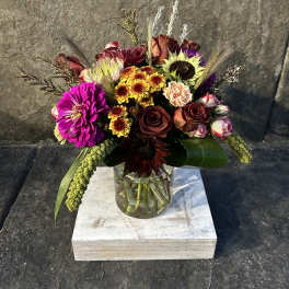 Mixed bouquet in a clear glass vase with bright blooms and dark roses