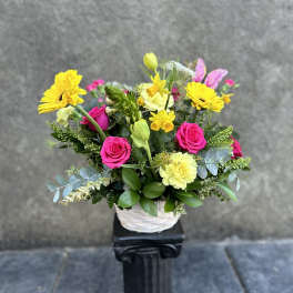 Bright mixed flower arrangement in a white basket with pink roses and yellow daisies