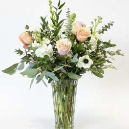 Peach and white roses in a clear glass vase with mixed greenery