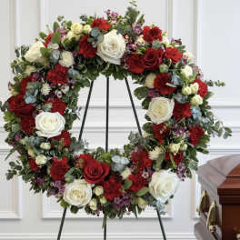 Circular funeral wreath of red and white roses on a stand