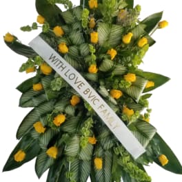 Standing floral spray with yellow roses and a white ribbon