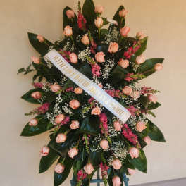 Standing floral wreath of pink roses with a white ribbon on an easel