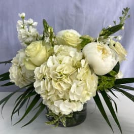 Low white arrangement of hydrangeas, roses, and peonies in a clear glass vase
