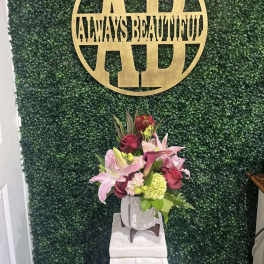 Pink lilies and roses arranged in a white vase on a pedestal