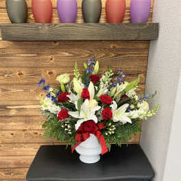 Red roses and white lilies arranged in a white vase with a red ribbon