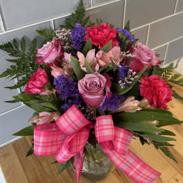 Bouquet of pink and purple flowers in a glass vase with a pink plaid ribbon