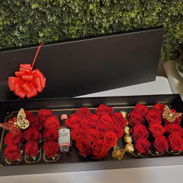 Black gift box filled with red roses, a wine bottle, and chocolates
