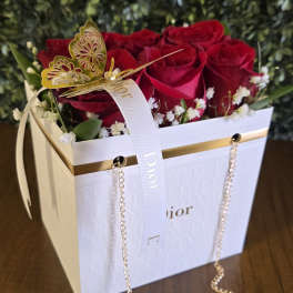 Red roses arranged in a white Dior gift box with a ribbon and gold butterfly decoration.
