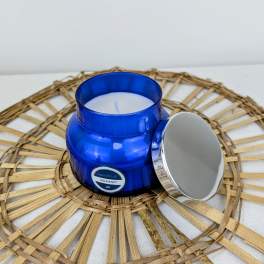 Blue glass candle jar with a silver lid on a woven mat