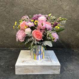 Pink and lavender mixed bouquet in a striped "let's celebrate" container