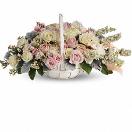 Low basket arrangement of pale pink and ivory roses with white accent flowers.
