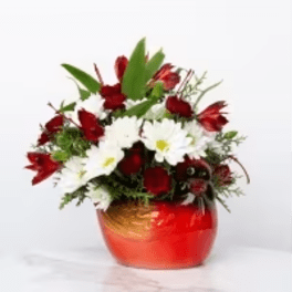 Red and white flower arrangement with daisies and roses in a round red ceramic bowl