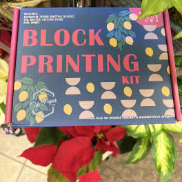 Block printing kit box surrounded by plants and red flowers