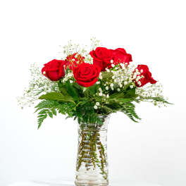 Red roses and small white flowers arranged in a clear glass vase