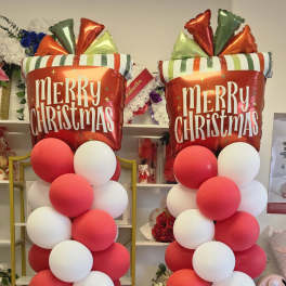 Two tall Christmas balloon columns with red and white balloons and Merry Christmas toppers