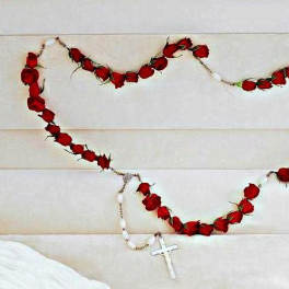 Red rose garland draped across a light upholstered headboard with a white cross necklace