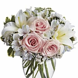 Rounded bouquet of pale pink roses and white lilies in a clear glass vase