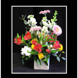 Mixed bouquet of pink, red, white, and yellow flowers in a white vase
