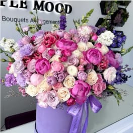 Large round arrangement of pink, lavender, and white blooms in a lavender hat box with ribbon.