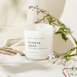 White flower shop candle in a glass jar with a floral sprig beside it