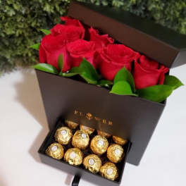Red roses in a black gift box above gold-wrapped chocolates