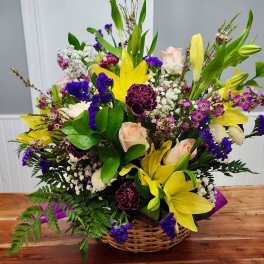 Basket arrangement with yellow lilies, pale roses, and purple flowers