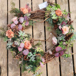 Floral wreath with peach roses, pinecones, and mixed greenery on a wooden surface